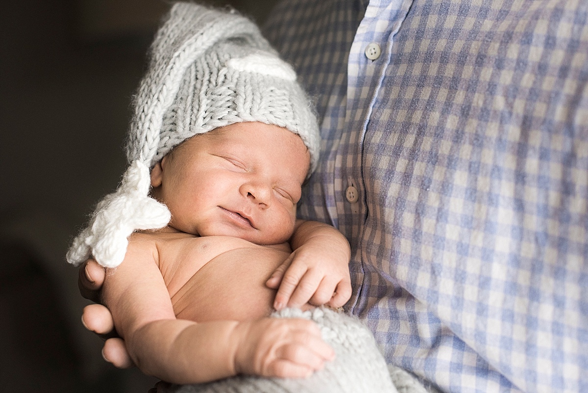 father holding newborn baby boy with blue hat