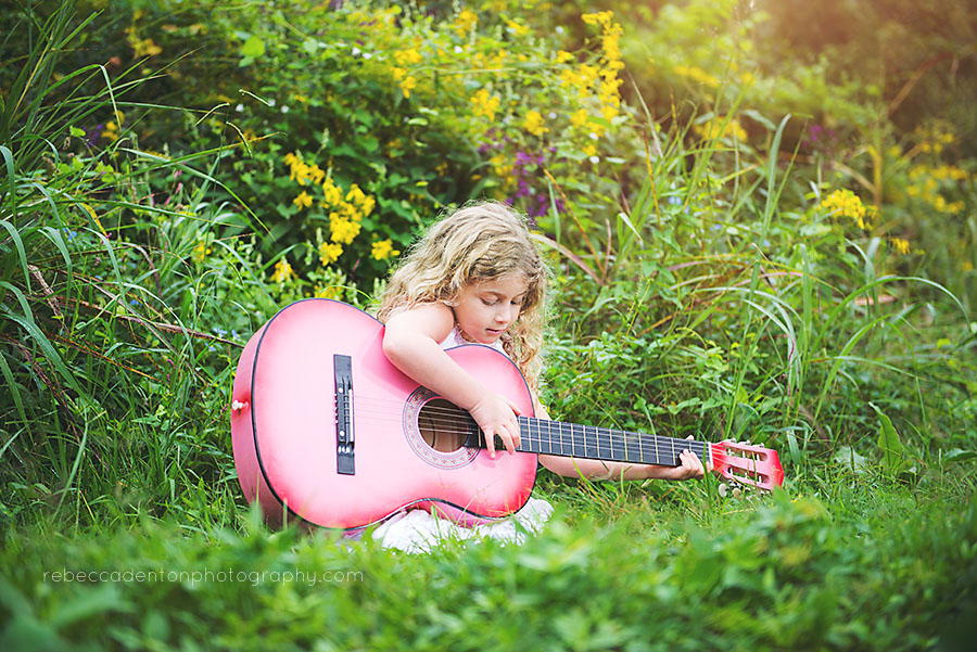 Little girl sitting in grass playing pink guitar