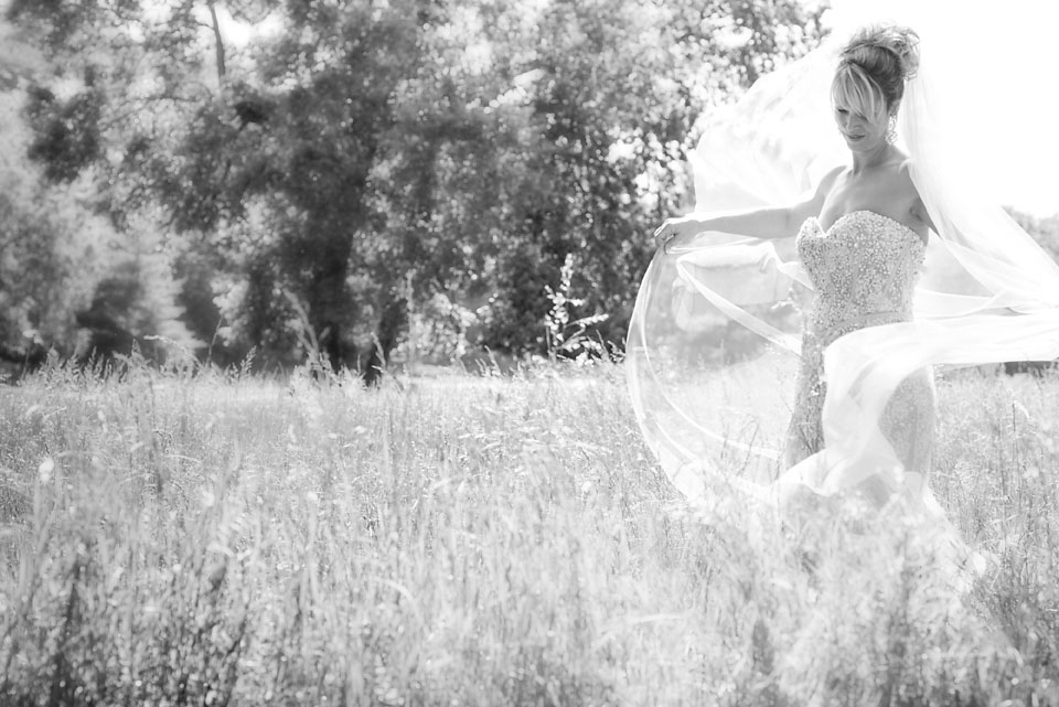 bride playing with veil in field with tall grass